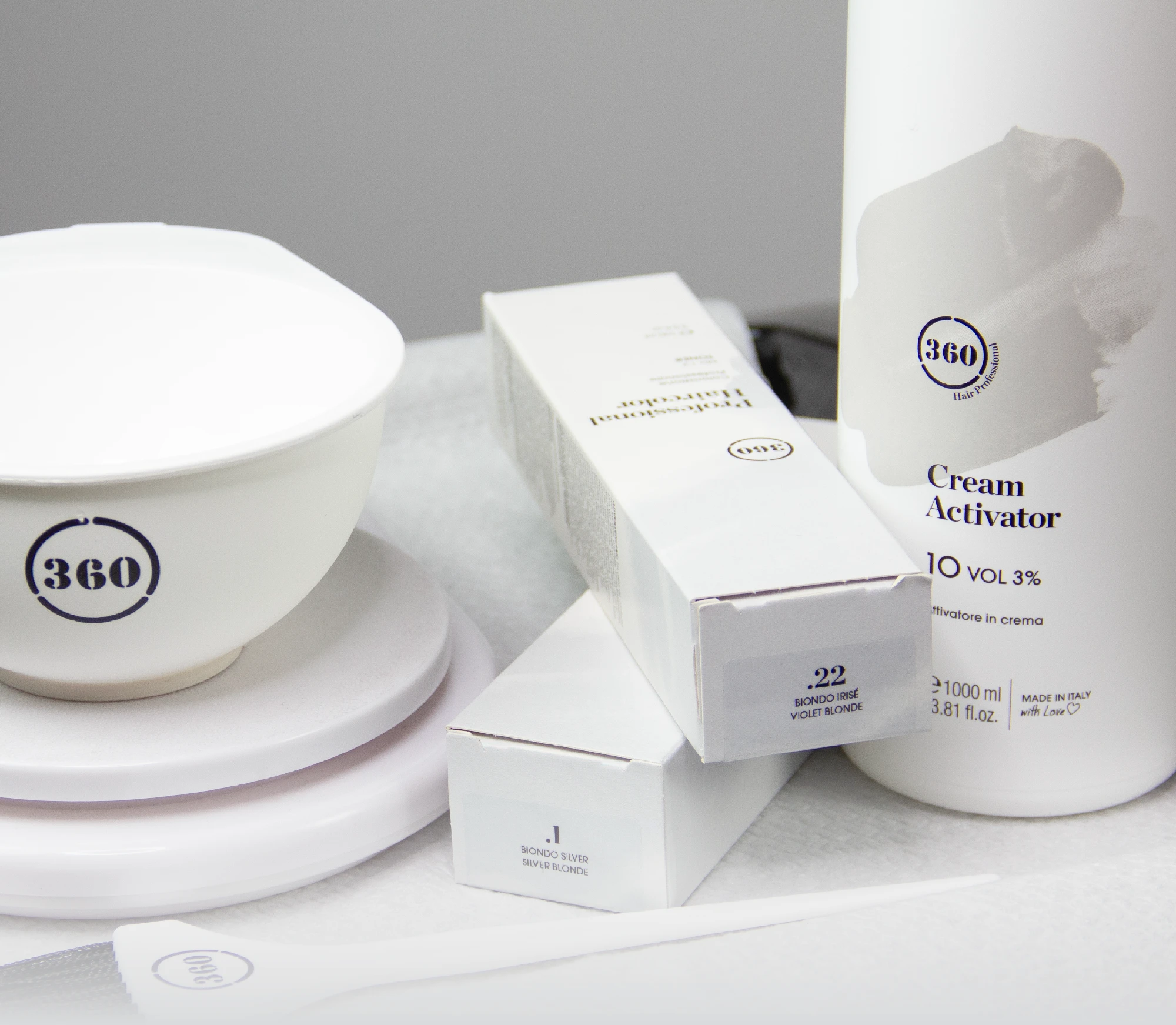 Professional hair coloring tools and products including a mixing bowl, boxes, spatula, and cream activator bottle arranged on a clean light surface.