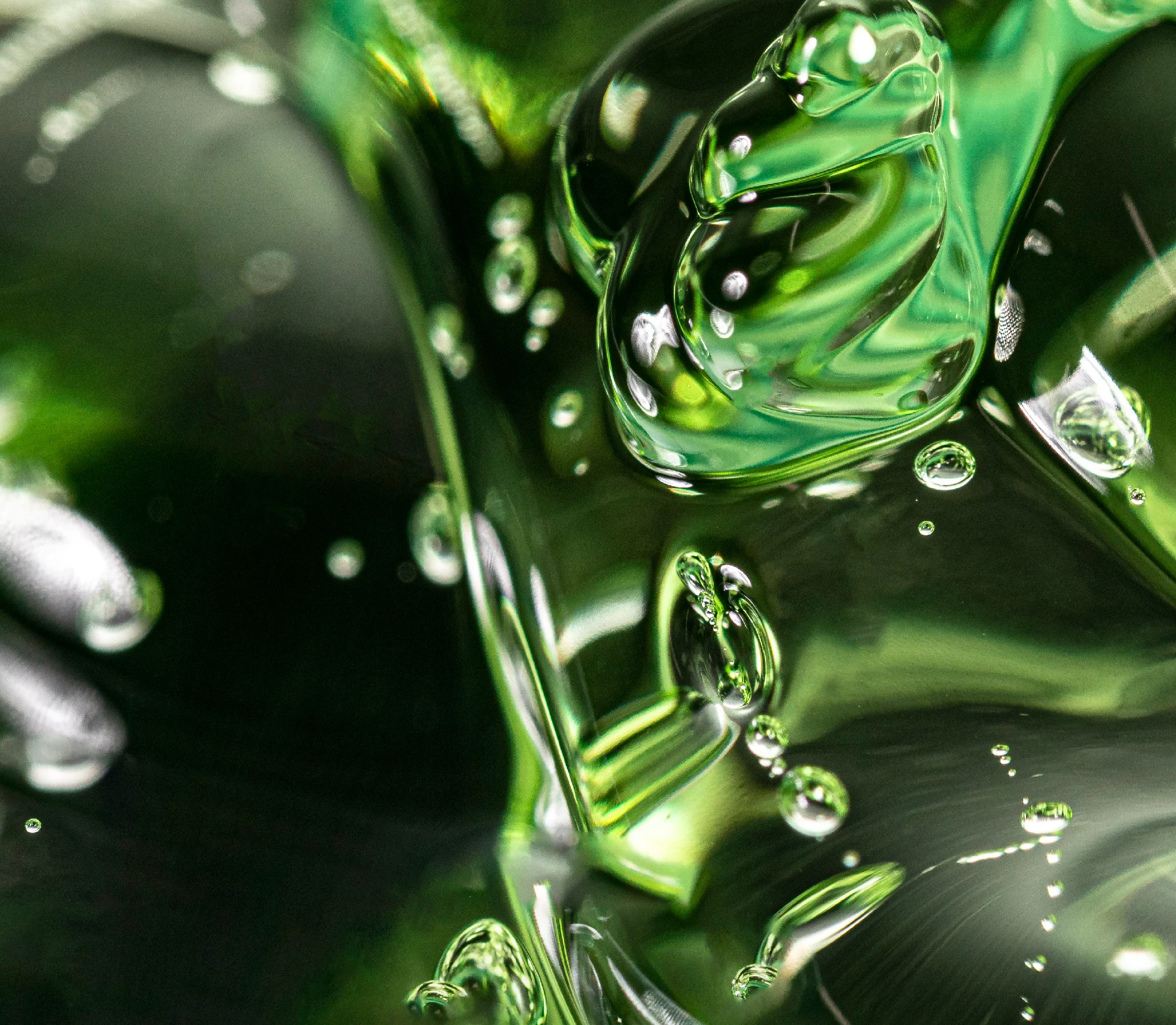Abstract close-up of glossy green gel with suspended air bubbles and fluid textures.